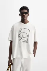 Camiseta blanca de corte relaxed fit, cuello redondo y manga corta. Presenta un bordado abstracto en color negro en el frente.