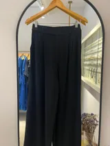 Pantalón sastrero negro de tiro alto, corte ancho y pierna recta. Presenta pliegues frontales y un detalle de cinturón fino a juego.