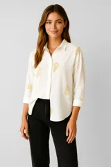 Camisa blanca de viscosa con bordados dorados de motivos orgánicos, corte holgado, cuello camisero y mangas largas con puños abotonados.