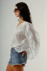 Blusa blanca de manga larga con volados en los puños y escote en V con botones frontales.