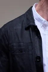 Campera tipo camisa de cuero negro con cuello clásico, cierre frontal con botones, bolsillos de parche en el pecho y corte recto.