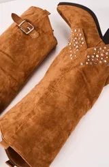 Bota texana de caña alta color camel, con detalles de tachas plateadas en el tobillo, hebilla decorativa y taco cuadrado.