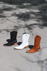 Botas texanas blancas de cuero con caña media, punta fina y cierre lateral. Presentan costuras decorativas en el empeine y el contorno de la caña.