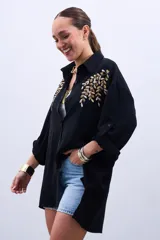 Camisa negra de mangas largas con puños abotonados y bordados dorados en el frente.