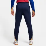 Pantalón largo de fútbol Nike FC Barcelona Strike para hombre, color azul marino con detalles en naranja. Presenta el escudo del club y el logo de Nike bordados.