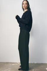 Pantalón negro de tiro alto con pinzas delanteras, pernera ancha y cinturón de cuero con hebilla dorada.