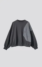 Buzo gris oscuro de cuello redondo, corte oversize y largo crop. Presenta un bolsillo grande de microfibra gris claro en el frente.