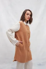 Camisa larga de lino color beige, con cuello camisero y cierre frontal con botones. Tiene mangas largas con puños abotonados, bolsillos laterales y una franja a contratono en la espalda y mangas.