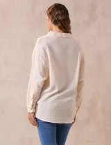 Camisa blanca de algodón con textura arrugada, cuello con solapa, abertura central con botones y bolsillo aplicado en el pecho. Mangas largas con largo regulable mediante presilla y botón.