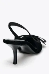 Zapato destalonado negro de terciopelo con tacón fino y tira trasera elástica. Detalle de lazo en la parte delantera.