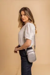 Bandolera pequeña tipo 'phone bag' de símil cuero color rosado pálido, con cierre de cremallera y correa ancha de tela con diseño de chevron en tonos claros.