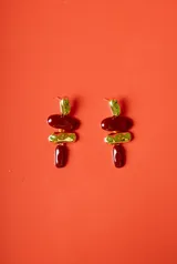 Aros colgantes con diseño de tres piezas: una pieza superior dorada irregular, una pieza central ovalada color bordó, una pieza intermedia dorada con textura y una pieza inferior alargada color bordó.