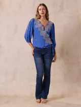 Blusa azul con bordados color crema, escote en V cruzado, mangas 3/4 abullonadas y nudo en el ruedo.