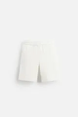 Bermuda relaxed fit color blanco confeccionada en tejido de algodón, con cintura elástica ajustable con cordón interior, bolsillos frontales y detalle de bolsillo trasero de plastrón.