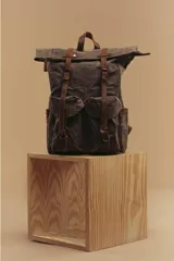 Mochila marrón de lona con detalles en cuero, cierre superior enrollable con hebillas y dos bolsillos frontales con hebilla.