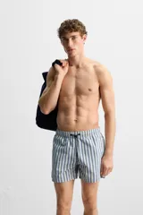 Bañador de hombre con rayas verticales azules y blancas, de corte medio, con cintura elástica ajustable con cordón, bolsillos laterales y trasero con solapa.