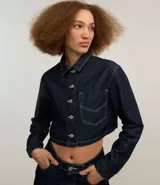 Camisa cropped de jeans azul oscuro, con cuello inglés, mangas largas, bolsillo en el pecho, pespuntes contrastantes y cierre con botones.