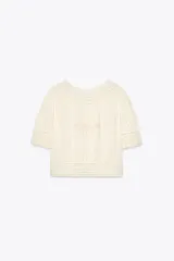 Blusa color crudo de cuello redondo y manga corta con puños. Presenta bordados a tono y cierre trasero con botones forrados.