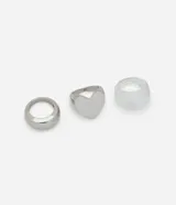 Set de tres anillos plateados y transparentes con diferentes diseños: uno liso, uno con forma de corazón y uno de resina transparente.