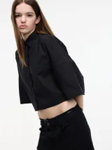 Camisa blanca cropped con botones en la parte delantera y mangas 3/4 con botones. Tiene pinza en la espalda.