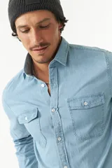 Camisa de jean azul de manga larga con dos bolsillos frontales con solapa abotonada.