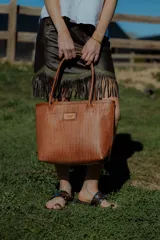 Bolso tipo tote de cuero color marrón con diseño tejido. Tiene bolsillo interno, porta llaves y cierre.