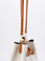 Cartera tipo bucket color blanco con base y lazo de ajuste color marrón.
