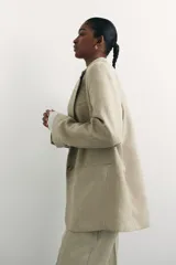 Blazer color beige de corte holgado con solapas de muesca, hombreras, abertura y botón en los puños, bolsillos delanteros ribeteados y bolsillo superior ribeteado. Forrado.
