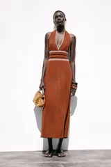 Bolso mini tipo saca de cuero serraje color marrón con efecto soft. Tiene doble asa de mano metálica dorada y asa bandolera extraíble. Cuenta con bolsillo interior con cremallera y cierre mediante fruncido y botón imantado.