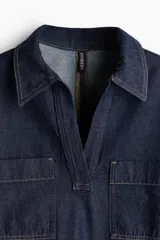 Vestido corto de denim azul oscuro, corte recto, con cuello camisero con escote en V, manga corta y dos bolsillos de parche en el pecho.