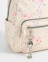Mochila urbana negra de cuerina con bolsillo frontal con cierre y charm colgante de cadena con dije de corazón y candado. Tiene correas regulables, manija superior, cierre superior, doble bolsillo frontal (uno con charm metálico) y bolsillos laterales.