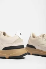 Zapatillas deportivas color beige con detalles en marrón y amarillo.