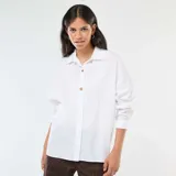 Camisa blanca de corte oversize, con cuello clásico, mangas largas y cierre frontal con botones fantasía dorados.