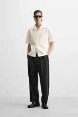 Camisa color blanco con textura de rayas verticales, corte relaxed fit, cuello bowling, manga corta, bolsillo de parche en el pecho y cierre frontal con botones.