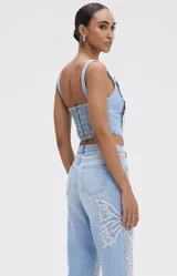 Top tipo corsé de denim celeste con diseño estructurado y varillas internas. Presenta un bordado artesanal de mariposa con cuentas en el centro.