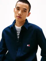 Camisa azul marino de algodón texturizado, corte oversize, cuello inglés, manga larga con puños abotonados, bolsillo de parche en el pecho con logo de Tommy Jeans bordado.