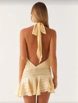 Minivestido color crema, con cuello halter, espalda descubierta, cintura elastizada y falda con volados.