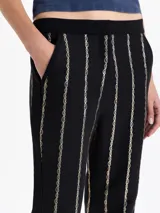 Pantalón negro de tiro alto con fit flare, confeccionado en jacquard con motivo de cadenas doradas que forman rayas verticales. Presenta tajos en los laterales del ruedo.