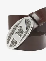 Cinturón de cuero bovino marrón con hebilla ovalada grande de metal plateado. La hebilla tiene un diseño con la letra 'D' en el centro, y el fondo está cubierto de pequeñas piedras brillantes.