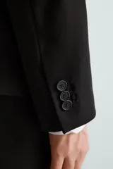 Blazer slim fit negra confeccionada en tejido con viscosa. Tiene cuello con solapas de muesca, manga larga con puño con detalle de botones, bolsillo de vivo en pecho, bolsillos de solapa en cadera, bolsillo interior, bajo con aberturas en espalda y cierre frontal con botones.