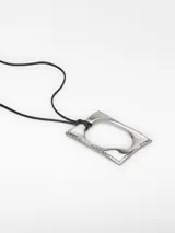Collar con cordón negro ajustable y colgante rectangular plateado con pieza ovalada blanca en el centro.