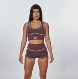 Conjunto deportivo color marrón, compuesto por un top con breteles anchos y logo 'bk.' estampado, y un short de calce ajustado.