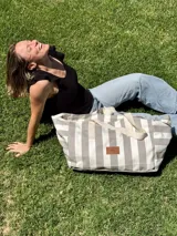 Bolso tipo tote extra grande de lona de algodón a rayas verticales grises y blancas, con asas de algodón color crudo y etiqueta de cuero con logo de la marca.