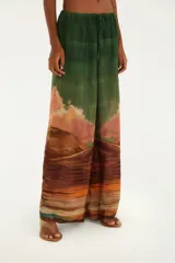 Pantalón palazzo con estampado de paisaje desértico en tonos verdes, marrones, naranjas y celestes. Presenta cintura alta con cordones ajustables.