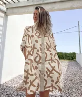 Vestido camisero de lino color beige con estampado abstracto en marrón. Tiene cuello camisero, cierre frontal con botones y mangas 3/4 con trabillas.