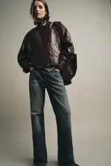 Chaqueta de Zara Woman Collection en tejido con acabado brillante efecto cuero. Presenta cuello solapa, manga larga con trabillas ajustables, bolsillos delanteros y cierre frontal con botones ocultos bajo solapa.