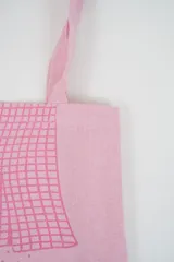 Bolso tote de tela con estampado de rayas verticales rosadas y blancas, laterales y asas en color beige. Presenta la palabra "BONJOUR" en verde en el centro y "INDIAN" en la parte inferior.