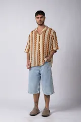 Camisa de manga corta con diseño de crochet a rayas verticales en tonos beige y marrón. Tiene cuello camisero y cierre con botones.