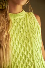 Chaleco marrón de punto con diseño trenzado, cuello redondo y sisas con volantes celestes.