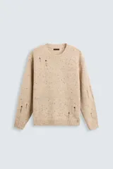 Sweater color beige con motas de colores, de tejido de punto grueso con cuello redondo y mangas largas. Presenta roturas y agujeros en el frente y las mangas.